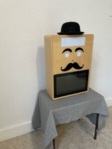 Photobooth Mister Moustache en bois, fabriqué artisanalement, avec chapeau et moustaches, vue de côté gauche